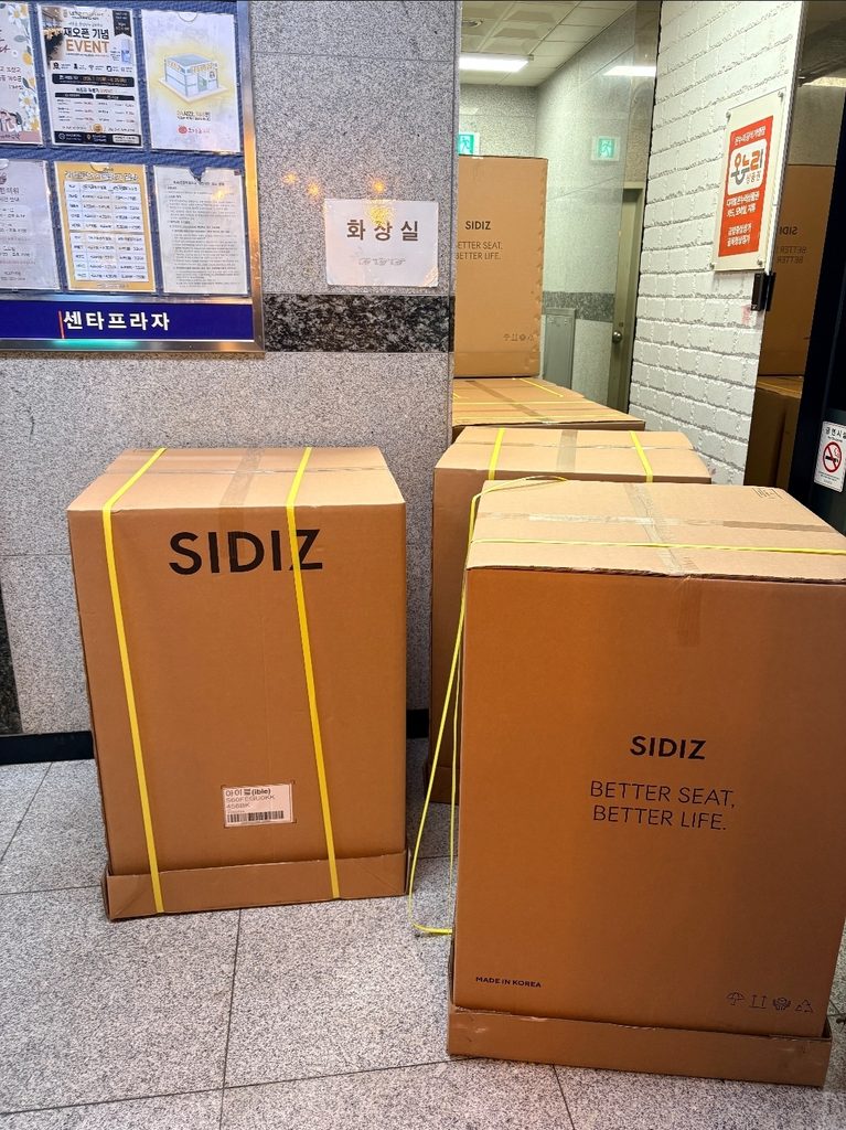 오산 세교지구 렛츠스터디카페 세교점의 환경 개선을 위해 대량으로 입고된 시디즈(SIDIZ) 의자 박스들. 복도에 쌓여있는 'BETTER SEAT, BETTER LIFE' 문구의 정품 박스 포장 상태. (오산 스터디카페 양도양수 매물)